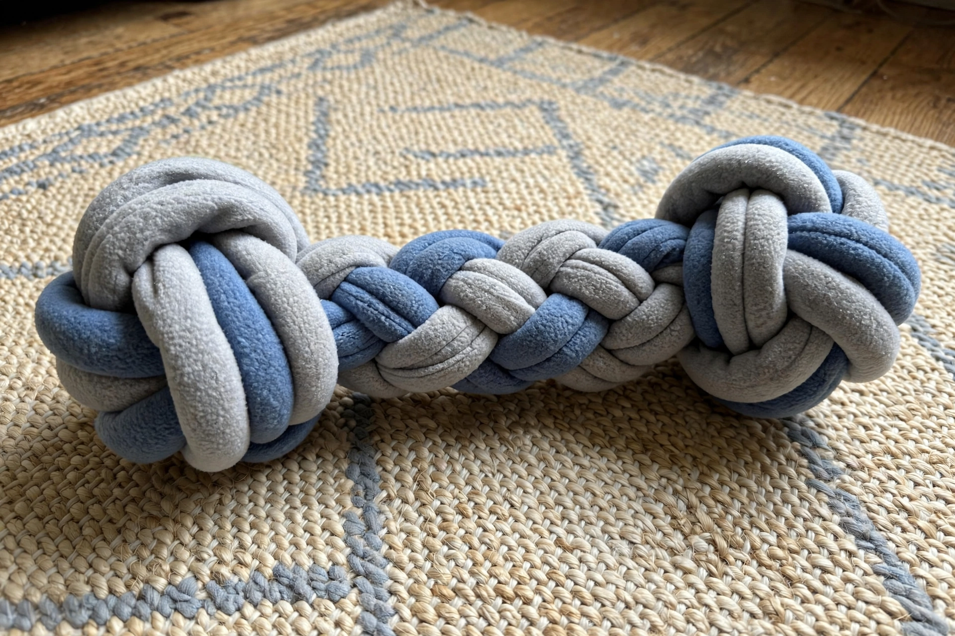 Handmade fleece dog bone toy with knots at each end on a rug